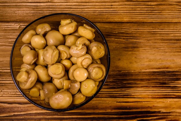 Glass bowl with canned mushrooms on rustic wooden table Top view