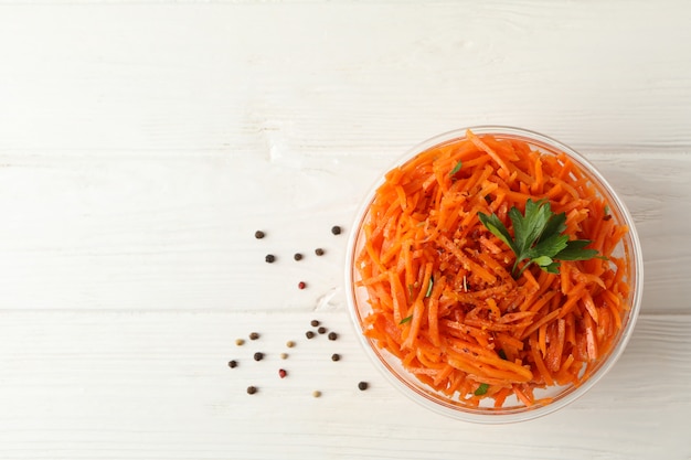 Glass bowl with carrot salad on white wooden background