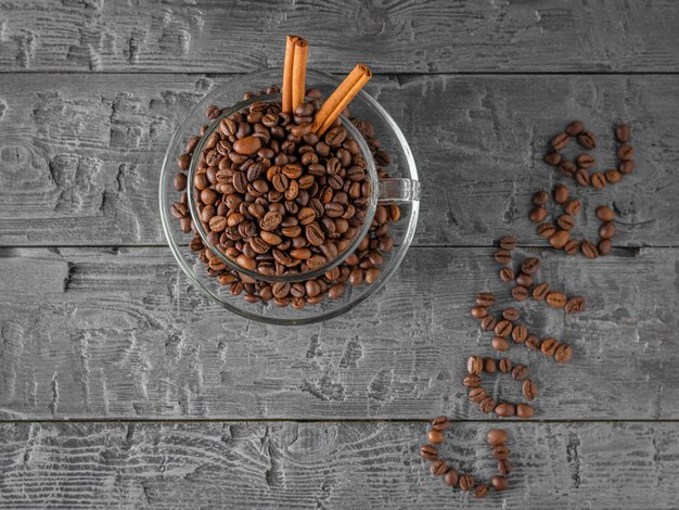 Glass bowl with coffee beans and cinnamon on black wooden table. The view from the top. Grains for the preparation of the popular drink.