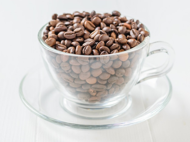 Glass bowl with coffee beans and cinnamon stick on white rustic wooden table.