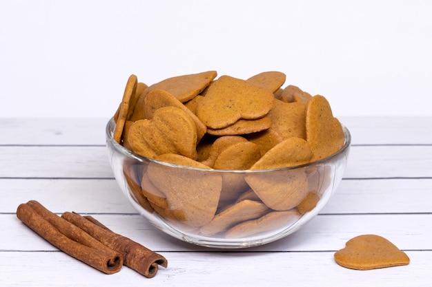 A glass bowl with crispy cookies in the shape of a heart and two cinnamon sticks