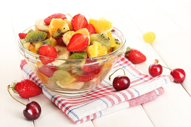 Glass bowl with  fresh fruits salad and berries on white wooden table