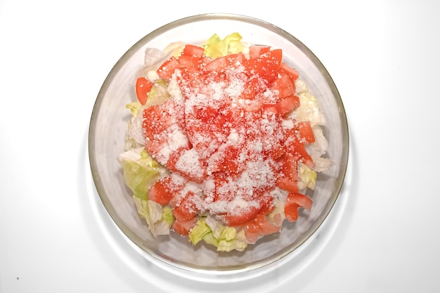 Стеклянная миска со свежим салатом айсберг, помидорами и тертым сыром. Ресторанное блюдо. Овощной салат.