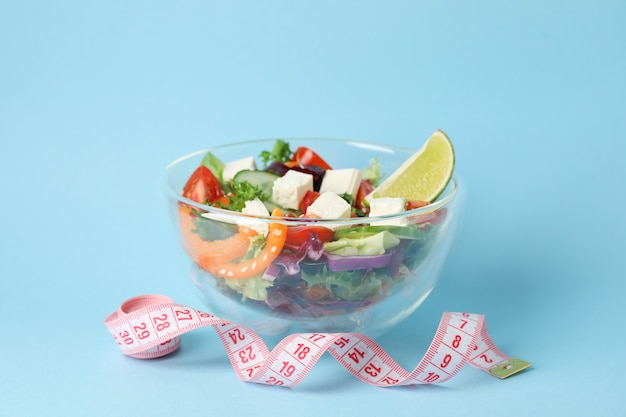 Glass bowl with fresh salad and measuring tape on blue