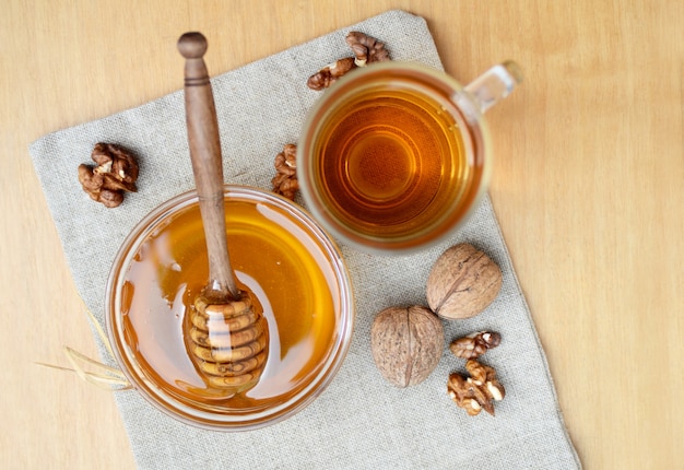 Glass bowl with honey and wooden stick, tea cup and walnuts