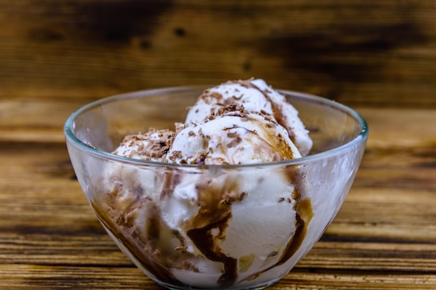 Glass bowl with ice cream balls and chocolate topping on a wooden table