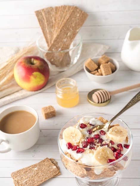 Ciotola di vetro con muesli e yogurt con banana, semi di melograno.