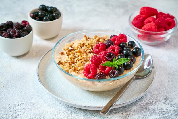 Стеклянная миска с овсянкой, разными ягодами и дроблеными орехами в стеклянной миске, здоровая сбалансированная еда