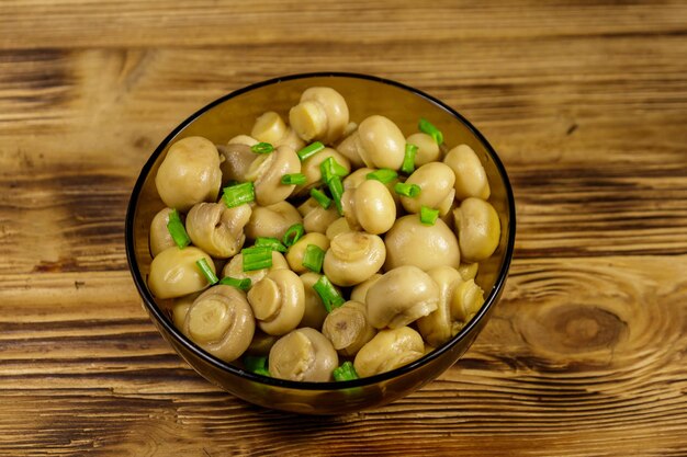 Glass bowl with pickled champignons Marinated mushrooms on wooden table