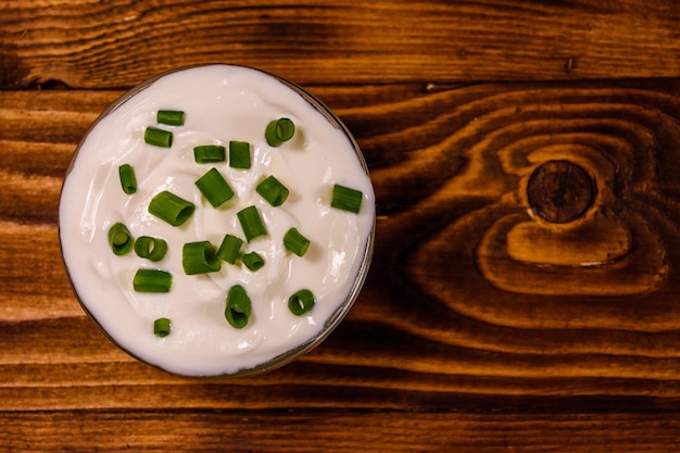 Photo glass bowl with sour cream and chopped green onion on rustic wooden table. top view