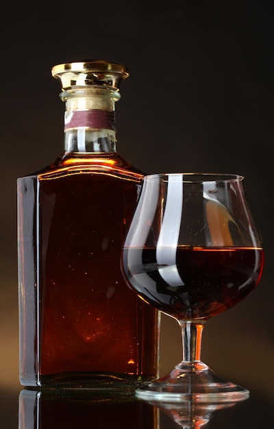 glass of brandy and bottle on brown background