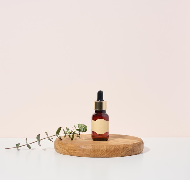 Glass brown bottle with a pipette on a wooden podium and a branch of eucalyptus