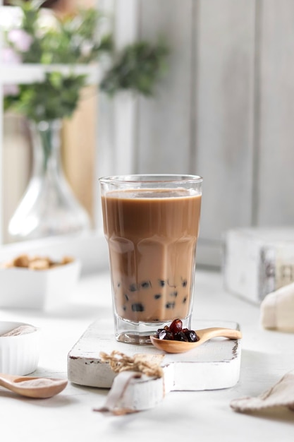 A glass of bubble tea sits on a table with a vase of almonds in the background.