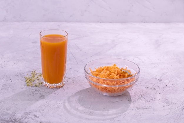 A glass of carrot juice and a glass bowl with carrot salad