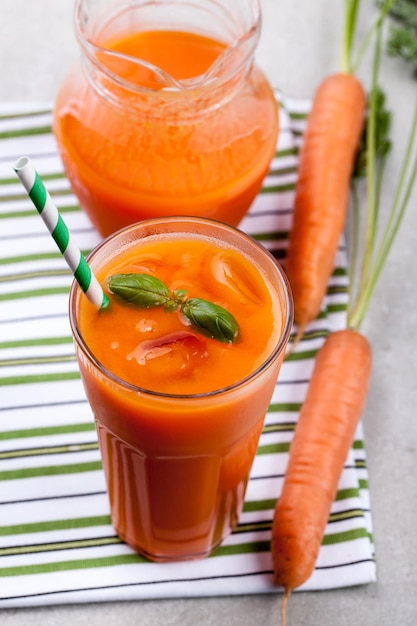 Glass of carrot juice, pitcher and fresh carrot on the table