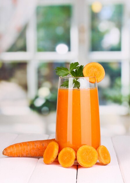 Glass of carrot juice on wooden table on window background