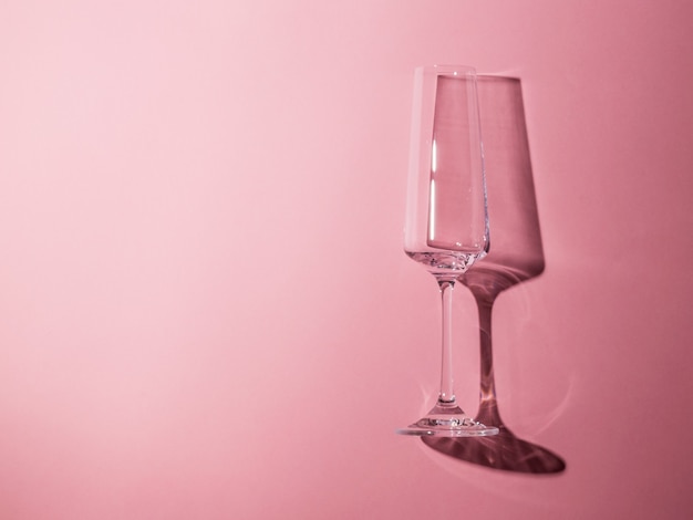 A glass of champagne on a pink background in bright light. Glassware in hard light.