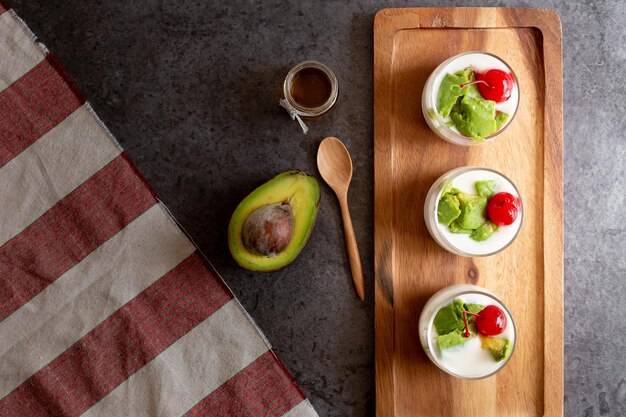 Photo glass of cherry and avocado sliced in yogurt on wooden background