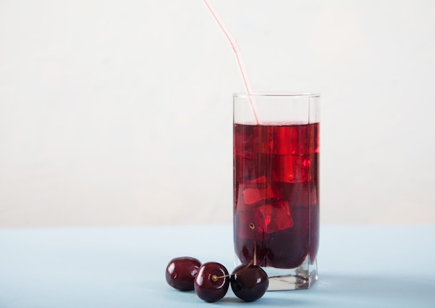 A glass of cherry juice with ice and cherries on a white table.