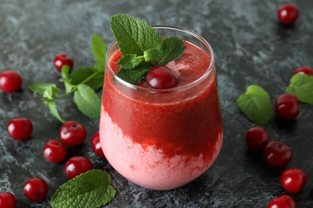 Glass of cherry smoothie and ingredients on black smokey table