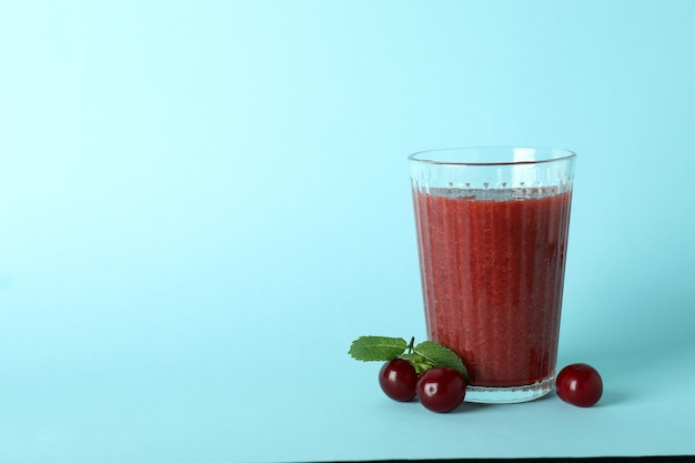 Bicchiere di frullato di ciliegie e ingredienti su sfondo blu