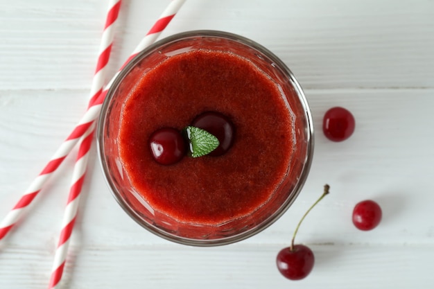 Photo glass of cherry smoothie, straws and ingredients on white wooden table