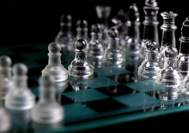 Glass chess pieces are defending the king on board in dark