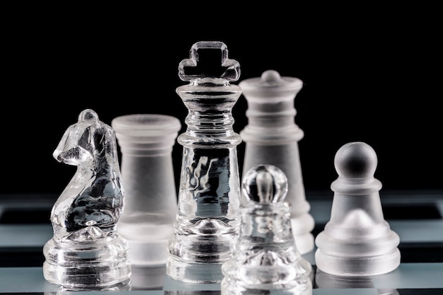 Glass chess pieces on a glass chessboard with reflection, on a black background.