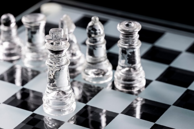 Glass chess pieces on a glass chessboard with reflection.