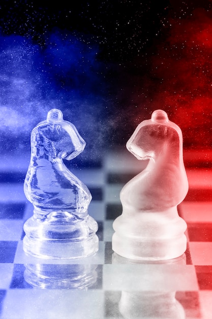 Glass chess pieces with blue and red light on a glass chessboard with reflection, on a black background.