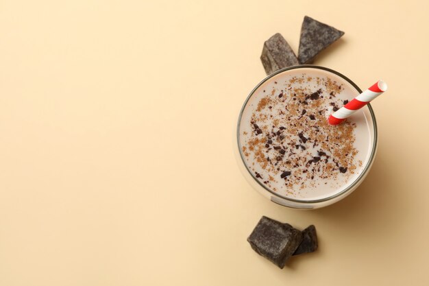 Glass of chocolate milkshake and chocolate pieces on beige background