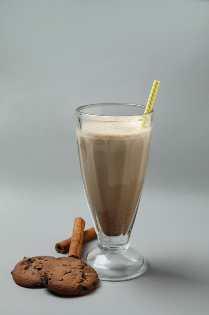 Glass of chocolate milkshake, cookies and cinnamon on gray wall