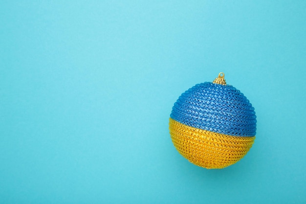 Glass Christmas ball toy on blue background with the flag of Ukraine