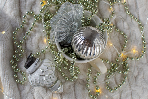 Glass Christmas toys and garlands in a white mug on a knitted plaid