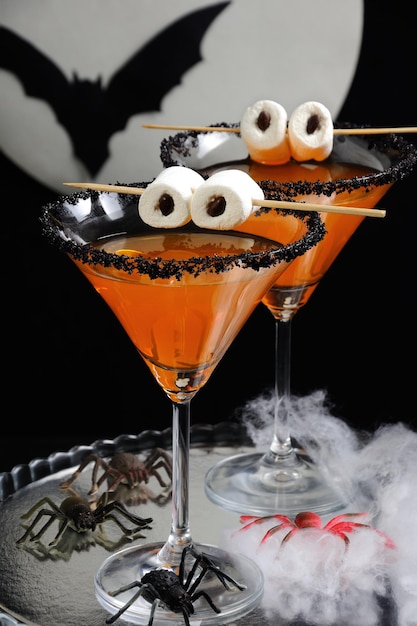 Glass of citrus martini decorated with black sugar with marshmallow eyes on the table in Halloween