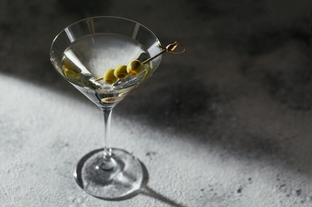 Glass of classic cocktail with olives on grey stone surface. 