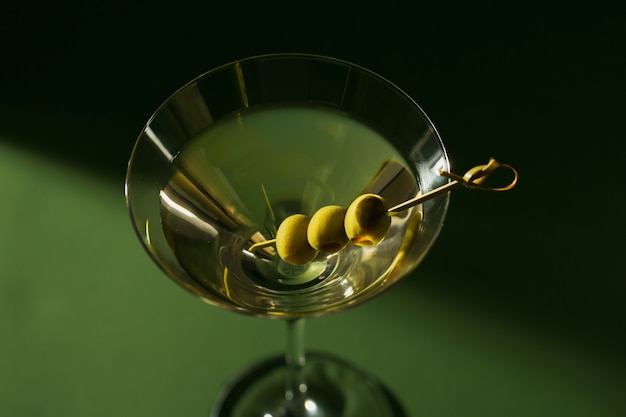 Glass of classic dry martini cocktail with olives on dark green