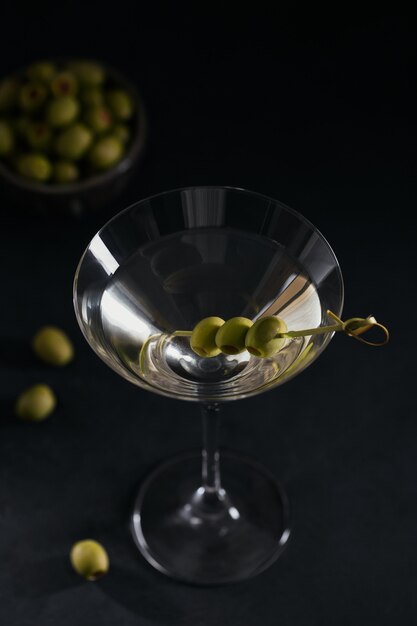 Photo glass of classic dry martini cocktail with olives on dark stone table against a black background.