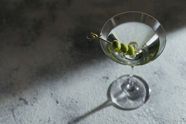 Glass of classic dry martini cocktail with olives on grey stone background