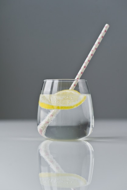 Bicchiere di acqua limpida con limone e paglia.