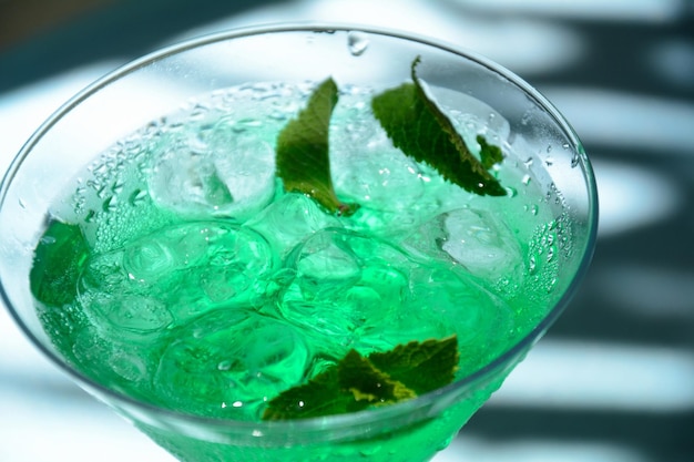 Bicchiere di fata verde da cocktail con limone e foglie di menta liquore alla menta dolce rinfrescante con ghiaccio e rum di assenzio cubetti di ghiaccio e vodka