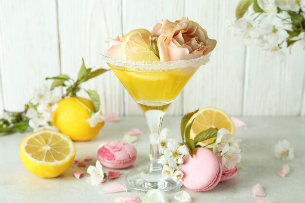 Glass of cocktail, ingredients and flowers against wooden background