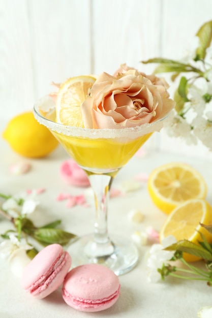 Glass of cocktail, ingredients and flowers on white textured table