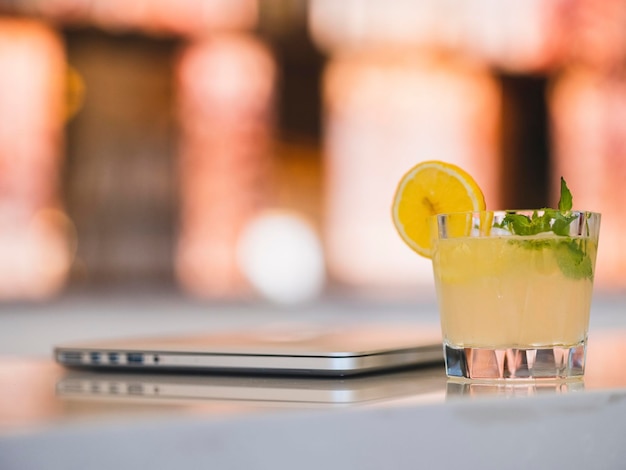 A glass of cocktail and laptop on a bar table