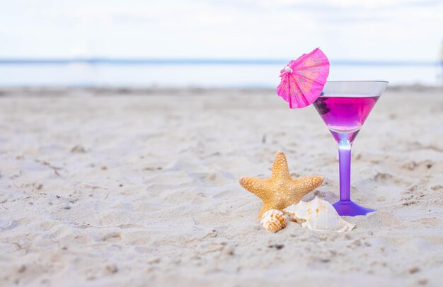 Glass of cocktail on sandy beach and starfish next to sea