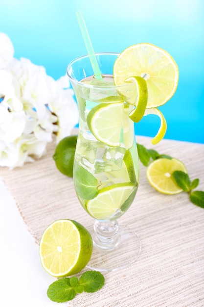 Glass of cocktail with lime and mint on table on light blue background