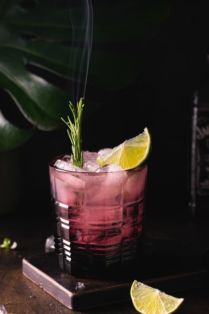 Glass of cocktail with smoked rosemary, lime and ice