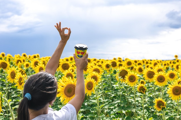 Glass of coffee in a female hand against the background of sunflowers