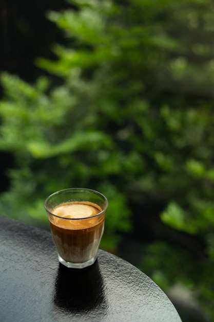 A glass of coffee sits on a table with a green background.