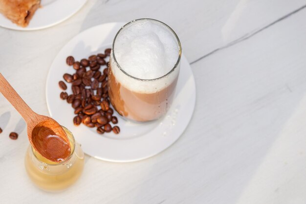 Glass coffee with foam milk with honey on white wooden table.